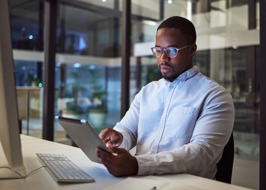 Businessperson with tablet in front of a desktop computer.