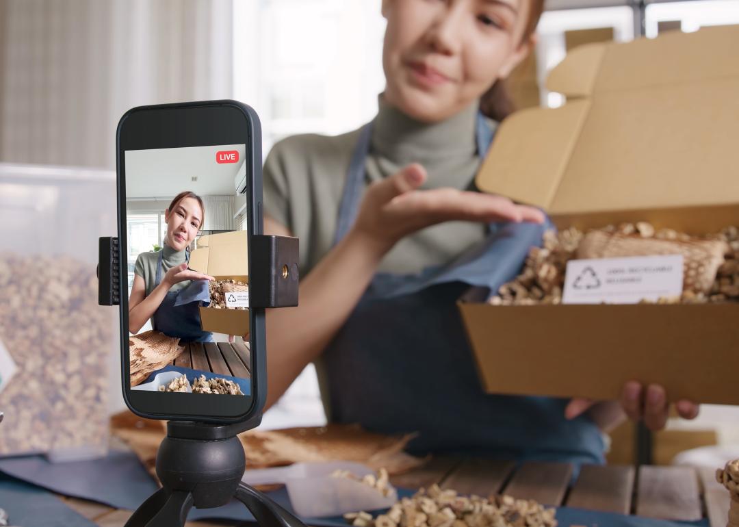 A social media influencer with her phone set up to record shows a package on a live video.