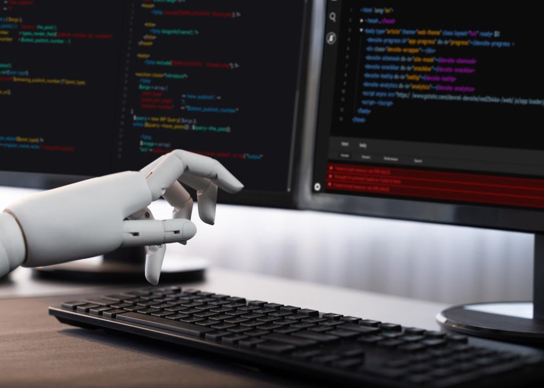 Robotic hand writing code on computer.