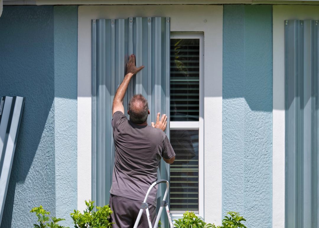 Home owner boarding up windows with steel storm shutters.