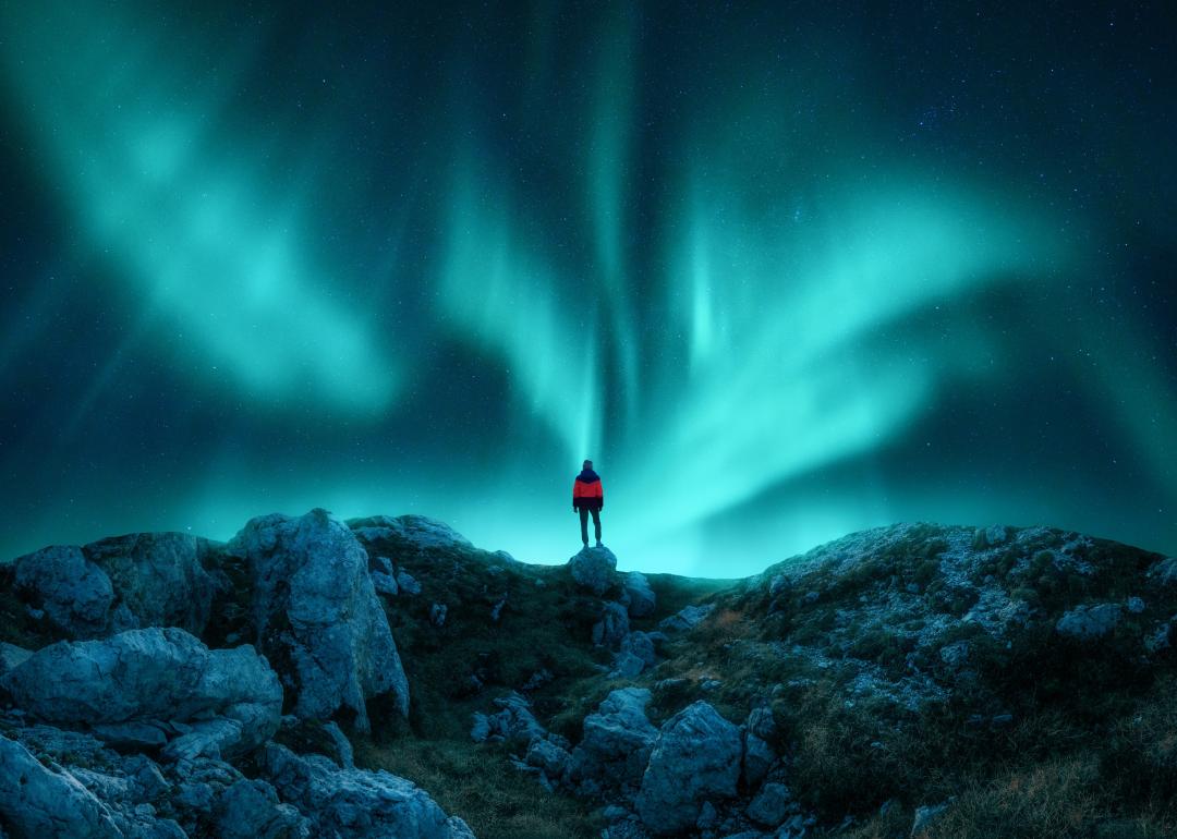 Aurora borealis and young woman on mountain peak at night.