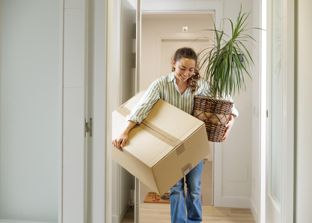 Woman arriving at a house with a plant and a box.