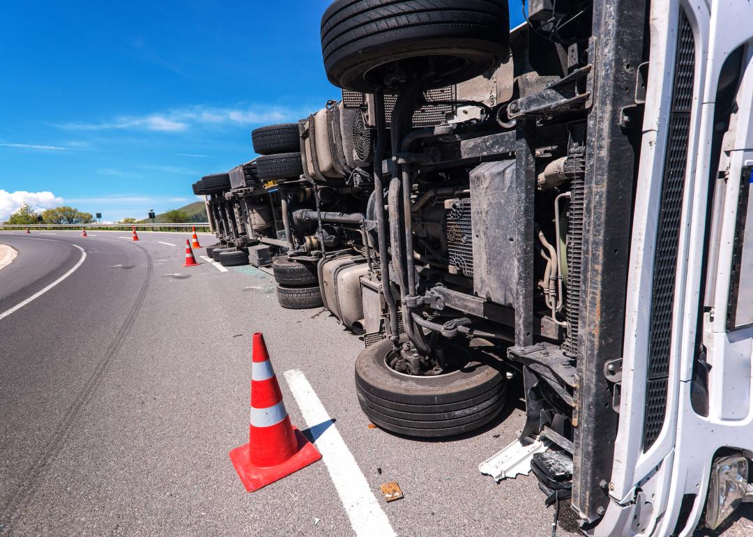 Crashed truck laying on its side on the side of the road.