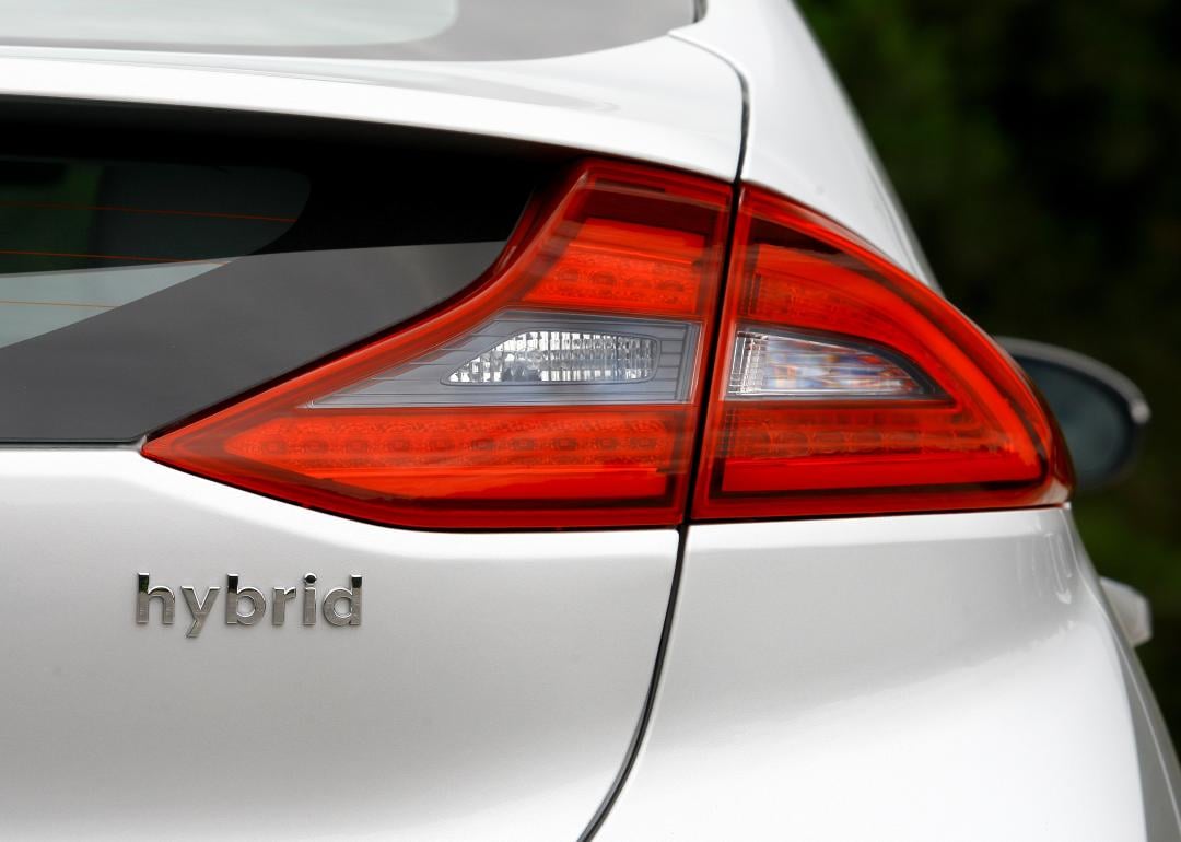 A close up view of the back of a white car with the word hybrid written under the tail light.