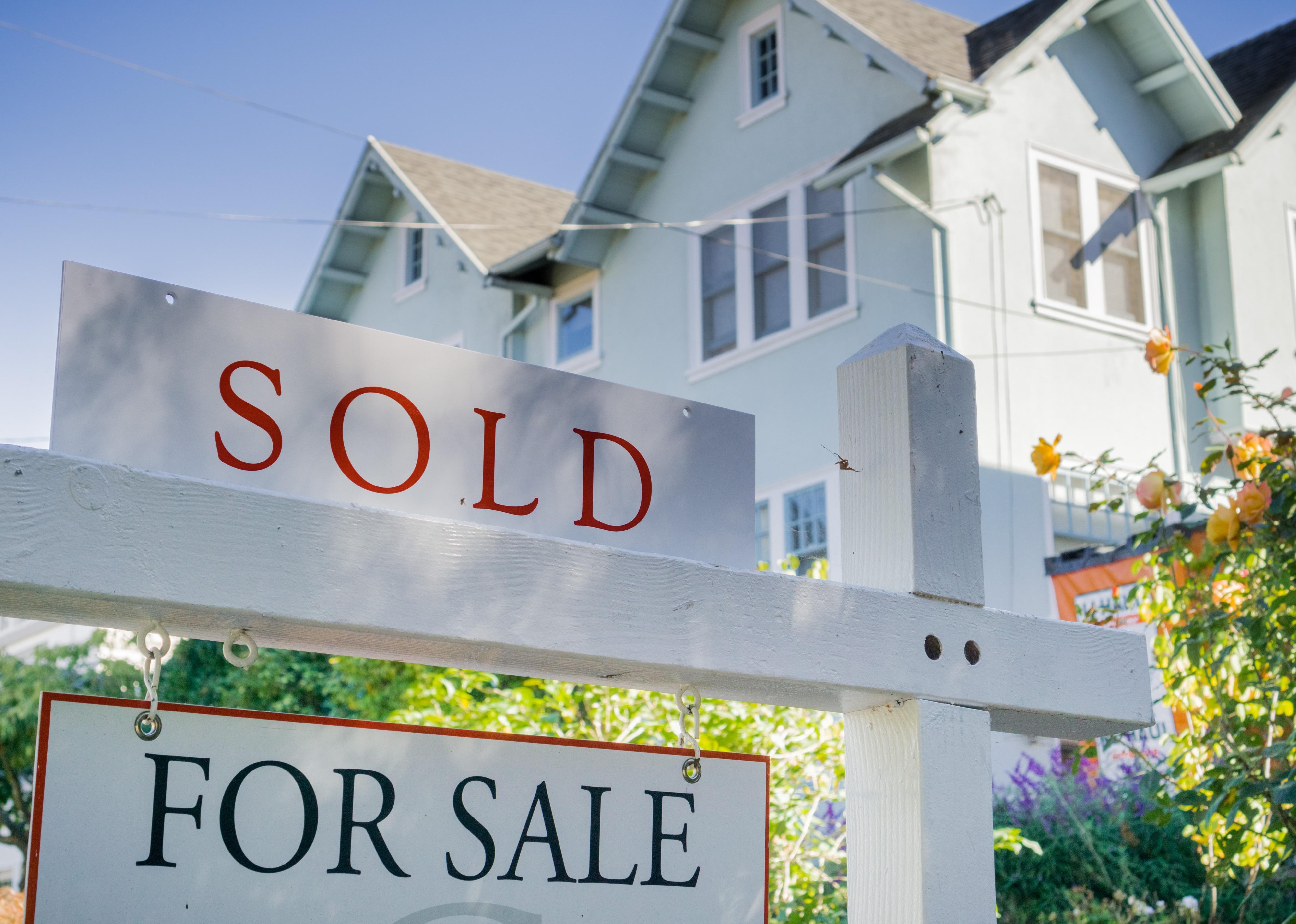 Sold sign in front of a house in a residential neighborhood.