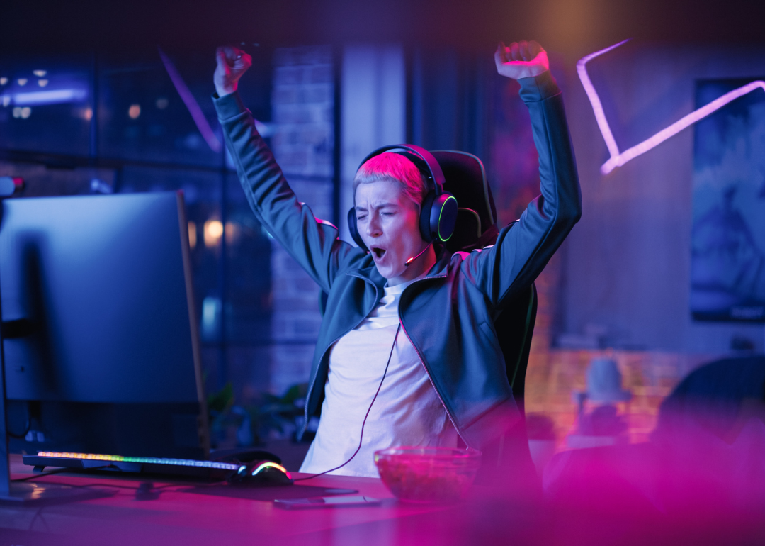 A person cheering at a computer in a dim room with neon lights.