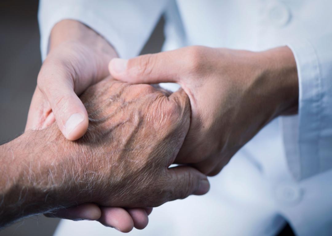 A medical professional holding an elderly pair of hands.