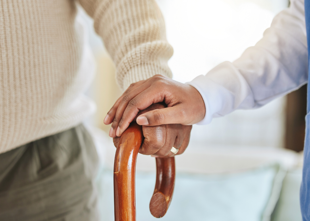 A nurse holding an elderly man's hand on his cane.