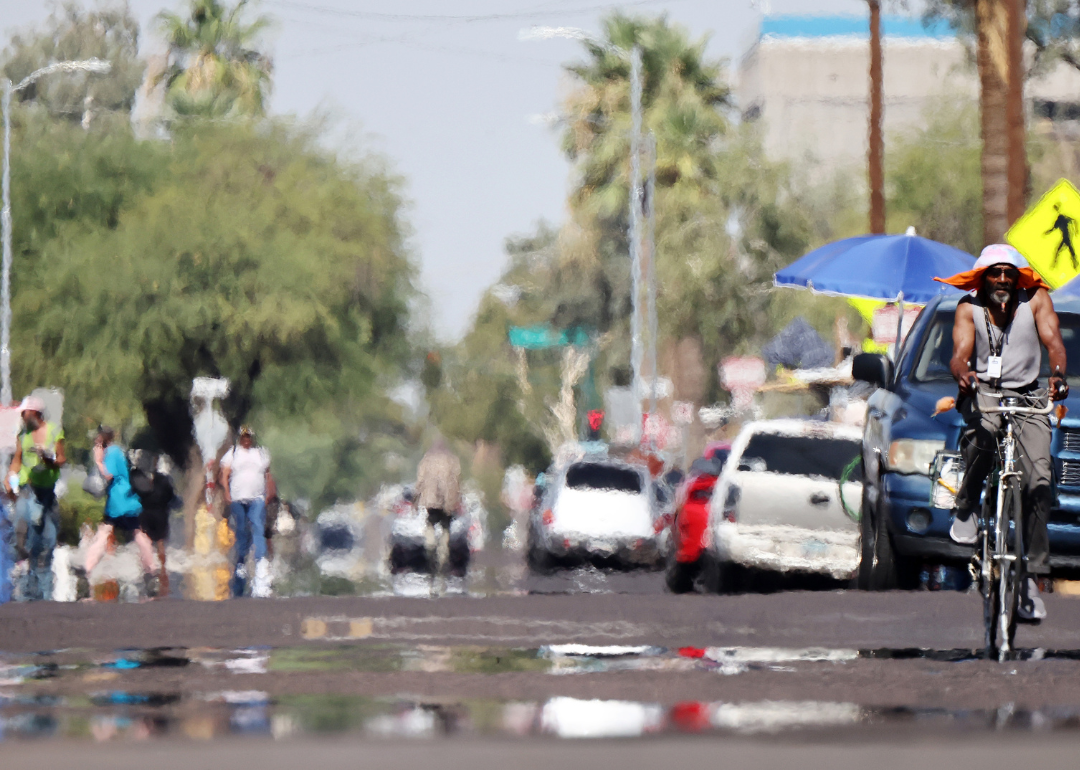 A heat haze above a busy road with people driving, cycling, and walking.