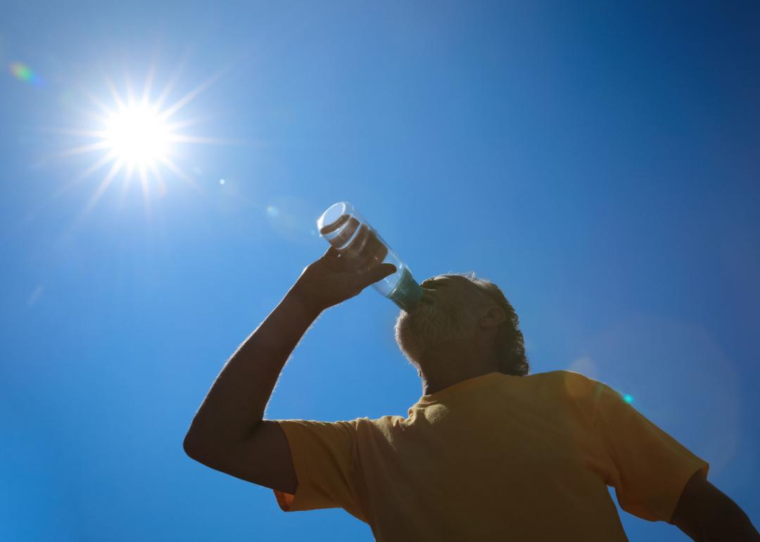 A person drinks from a water bottle as the sun shines in the blue sky.