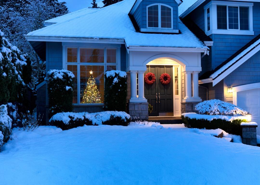 A home in the snow with a Christmas tree in the window.