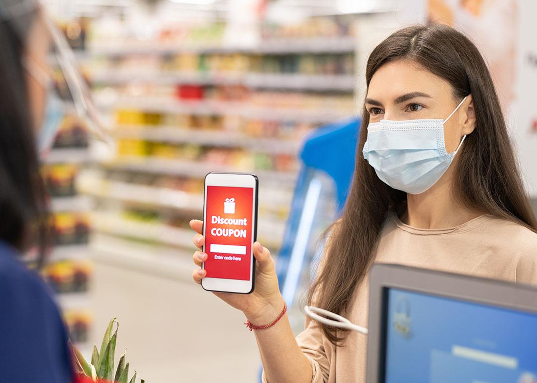 Woman holding up a smart phone with red discount coupon displayed with and drugstore shelves in the background.