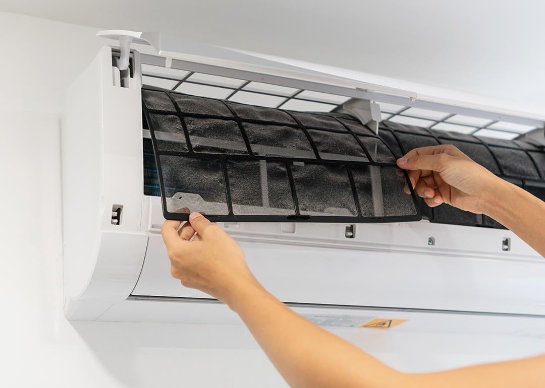 Person pulling out a dirty air conditioner filter from a mini-split unit.