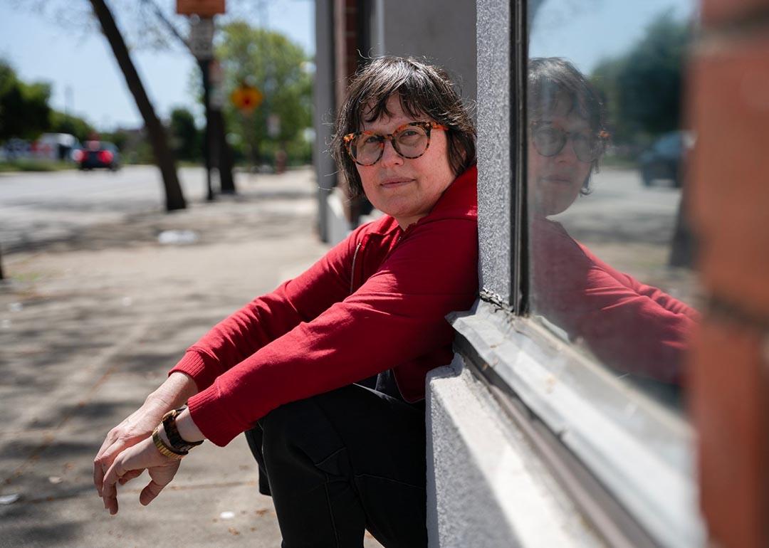 Julie Crossman sitting on a stoop wearing a red long-sleeve shirt, is the sister of Nanie Crossman who she lost touch with, in Oakland on April 8, 2025