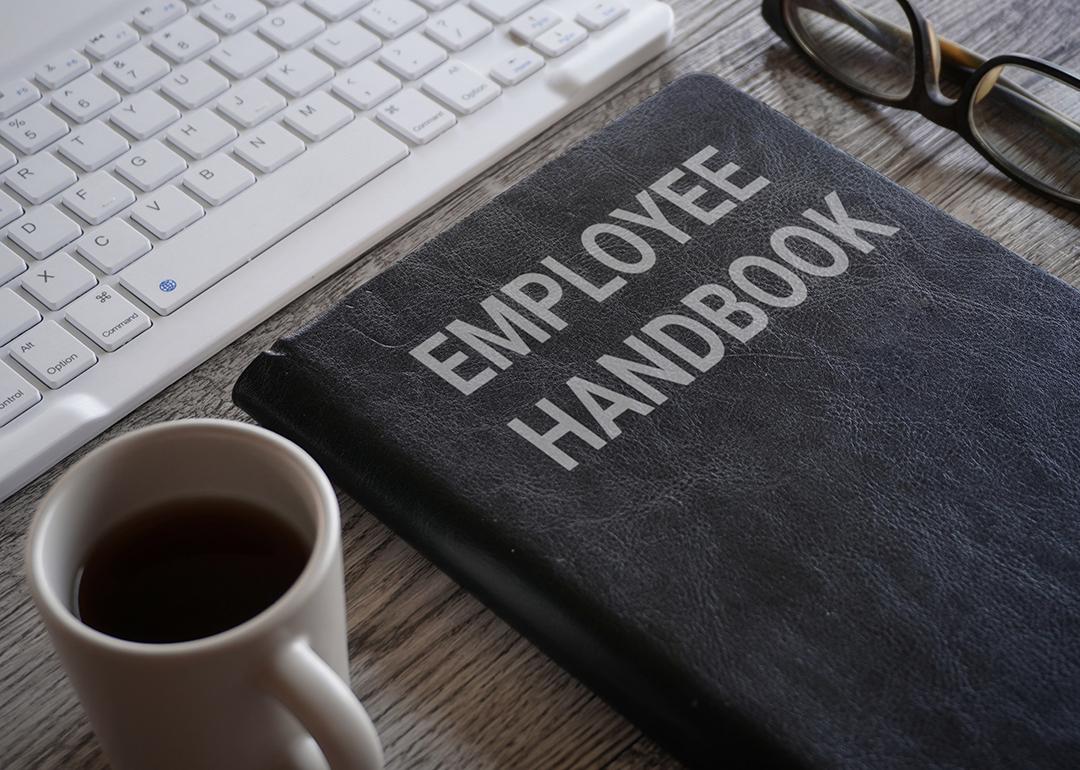 An employee handbook and a cup of coffee in front a work computer keyboard.