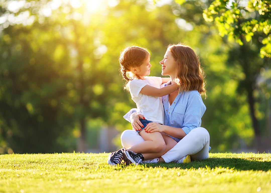 A mother with her young daughter sitting on grass in a nature park.