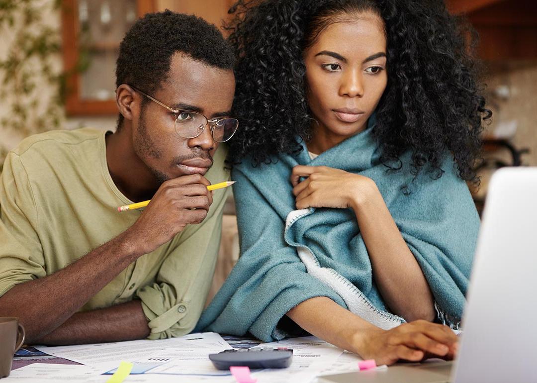 Young Black couple looking over laptop screen with papers and a calculator sitting on the table