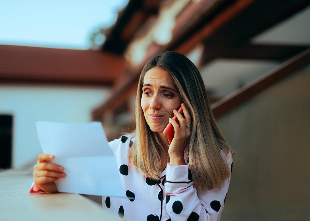 An emotional woman looking at her credit card bill while on the phone.