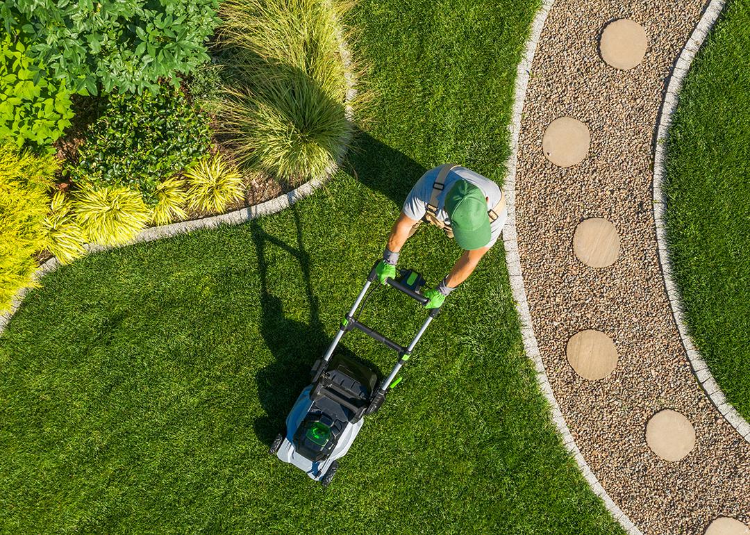 High-angle view of a gardener mowing a backyard using a cordless electric mower.