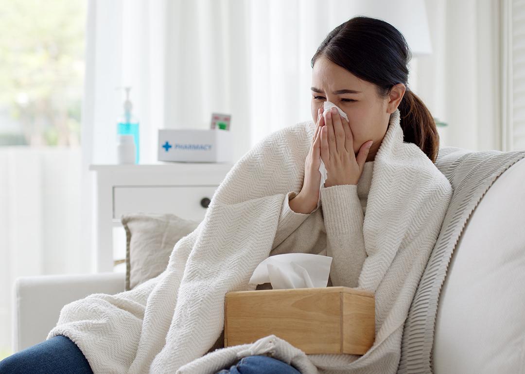 Young woman with a cold sitting under a blanket on a sofa.