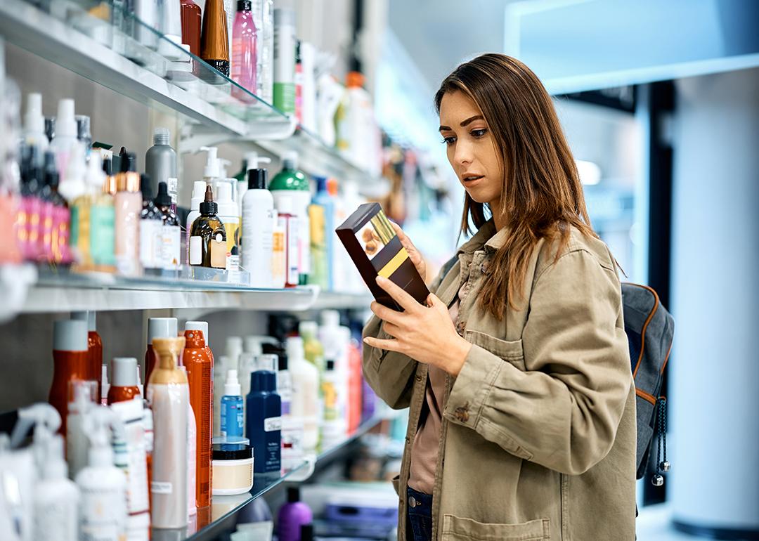 Young woman reading the label of a skincare product in a shopping mall.