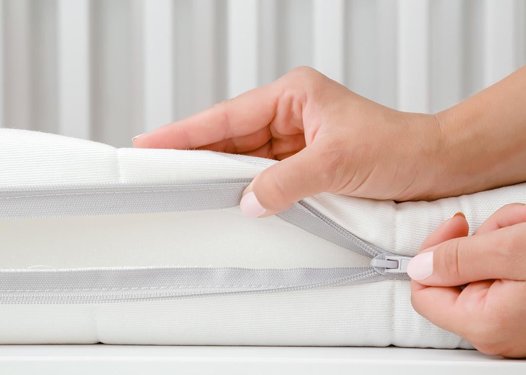 A woman's hand opening the cover of new white mattress to check the quality of a baby's bed.