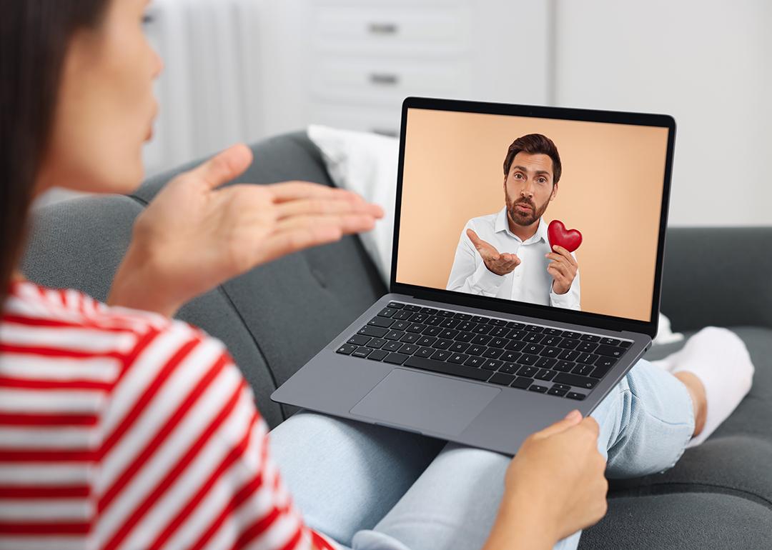 Concept of romance scam illustrated by a couple communicating long-distance via video chat, with man holding a heart figure and blowing a kiss.