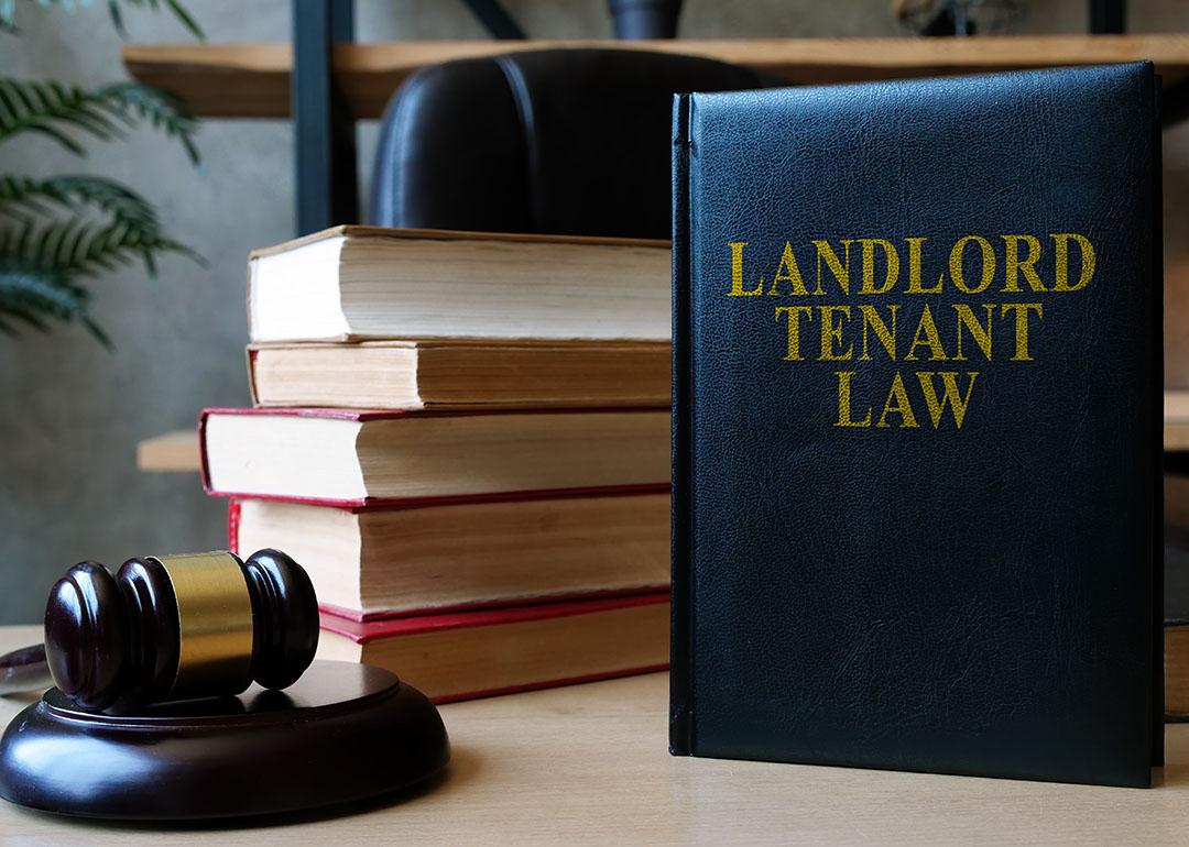 A desk with a judge's gavel on the left, a pile of books with the spines facing away from the camera and a blue book standing upright titled "Landlord Tenant Law" in gold letters.