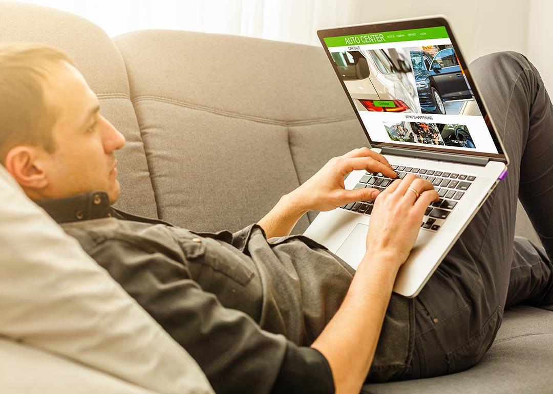 Man lying on sofa while using his laptop to browse for cars online.