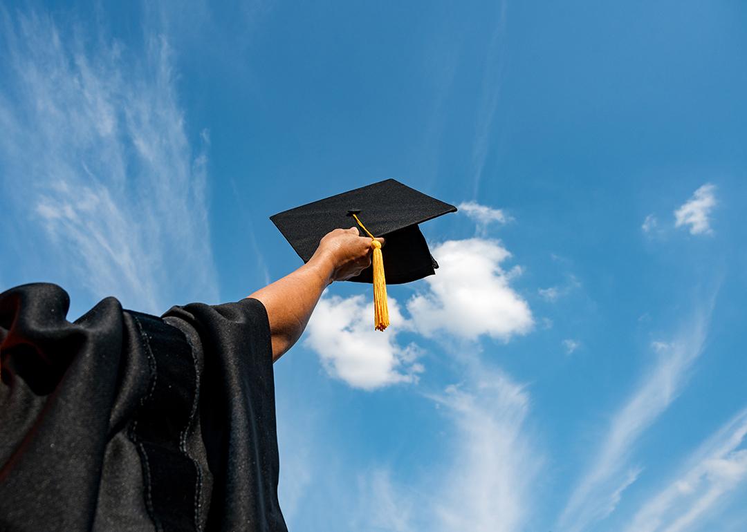 A graduate student holding up a graduation cap in the sky.