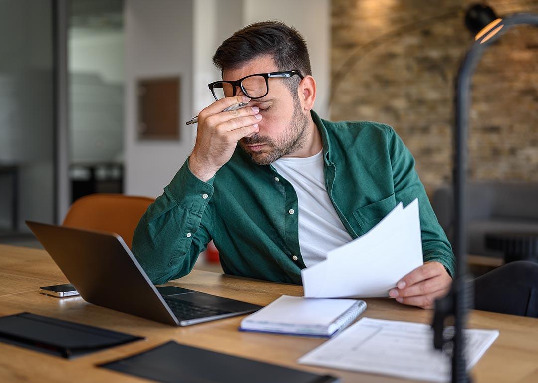 Anxious landlord rubbing eyes while looking at documents.