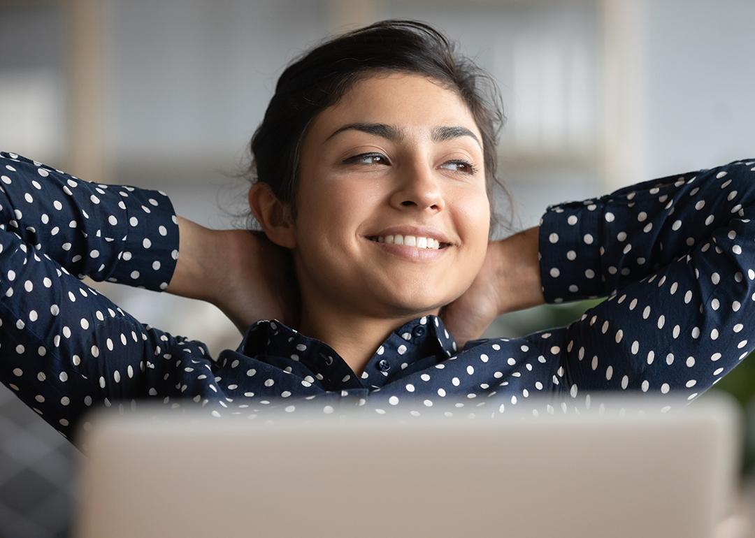 Satisfied woman happily sitting at work with her hands behind her head.