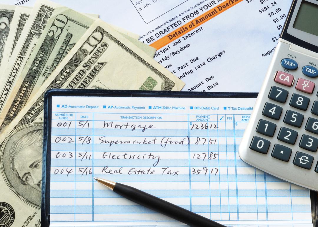 Balancing a checkbook with U.S. bills and calculator and bills visible on a table.