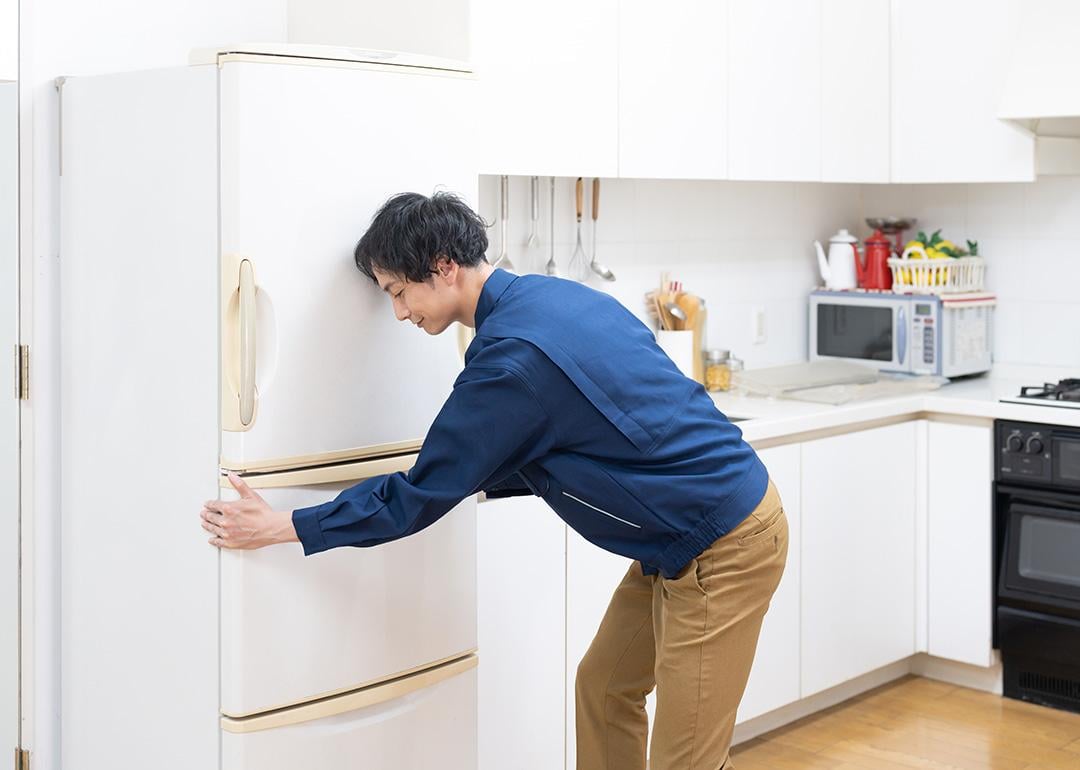 Man fixing the placement of his fridge in the kitchen.