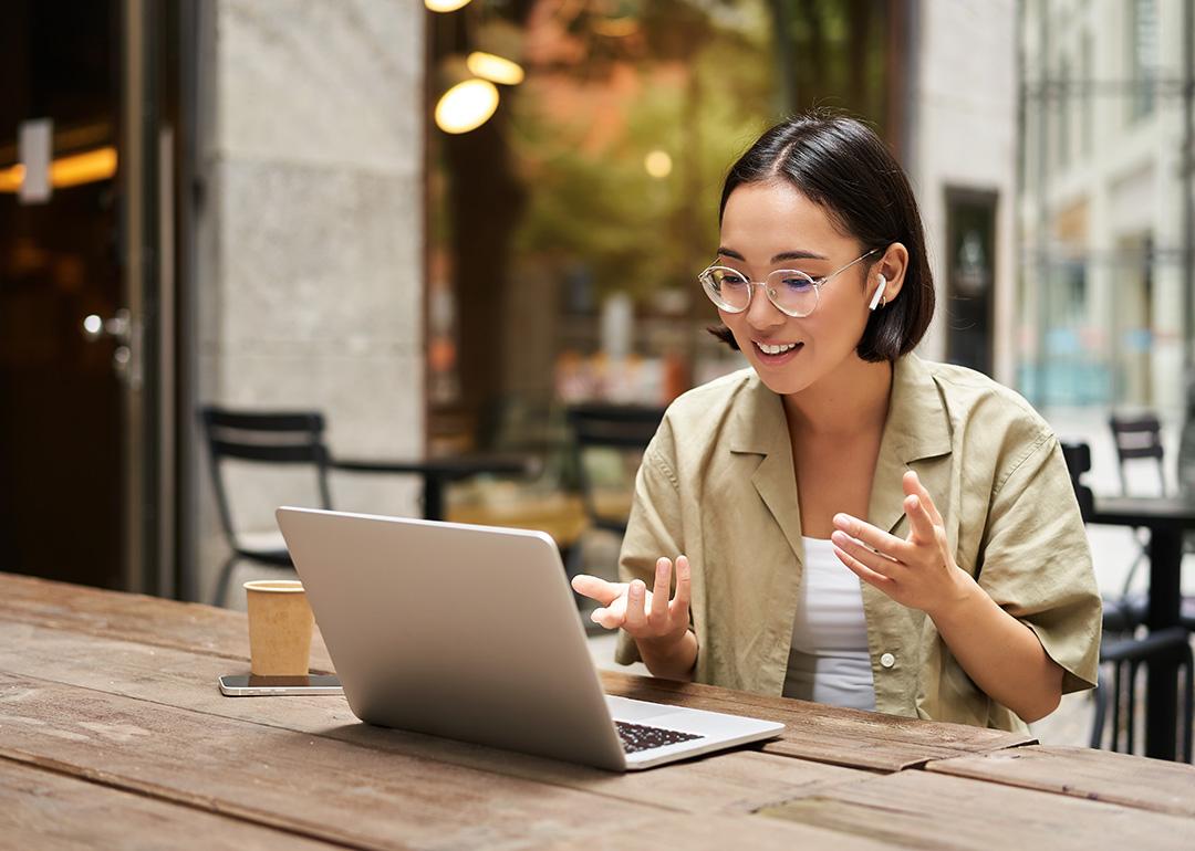 A young woman working remotely in an outdoor cafe, engaged in a virtual meeting.