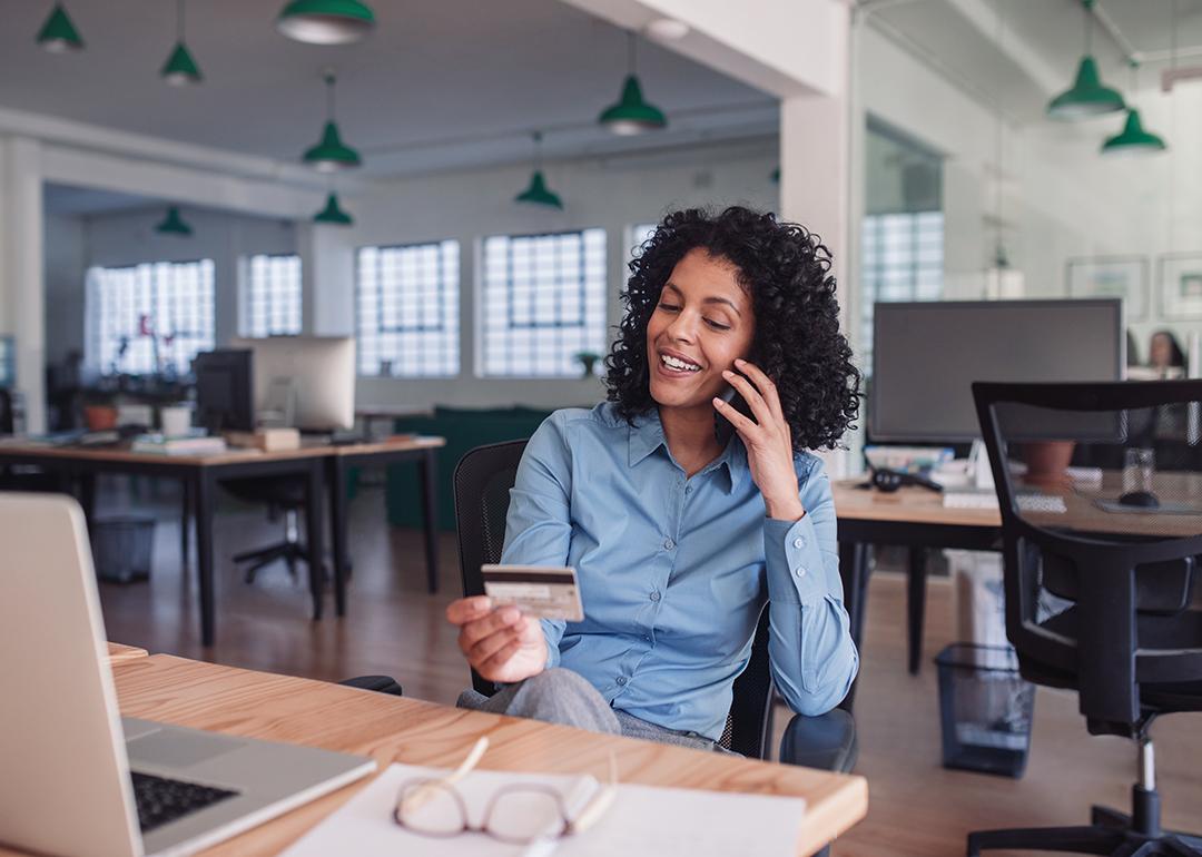 Businesswoman in her workplace looking at her credit card while on the phone.