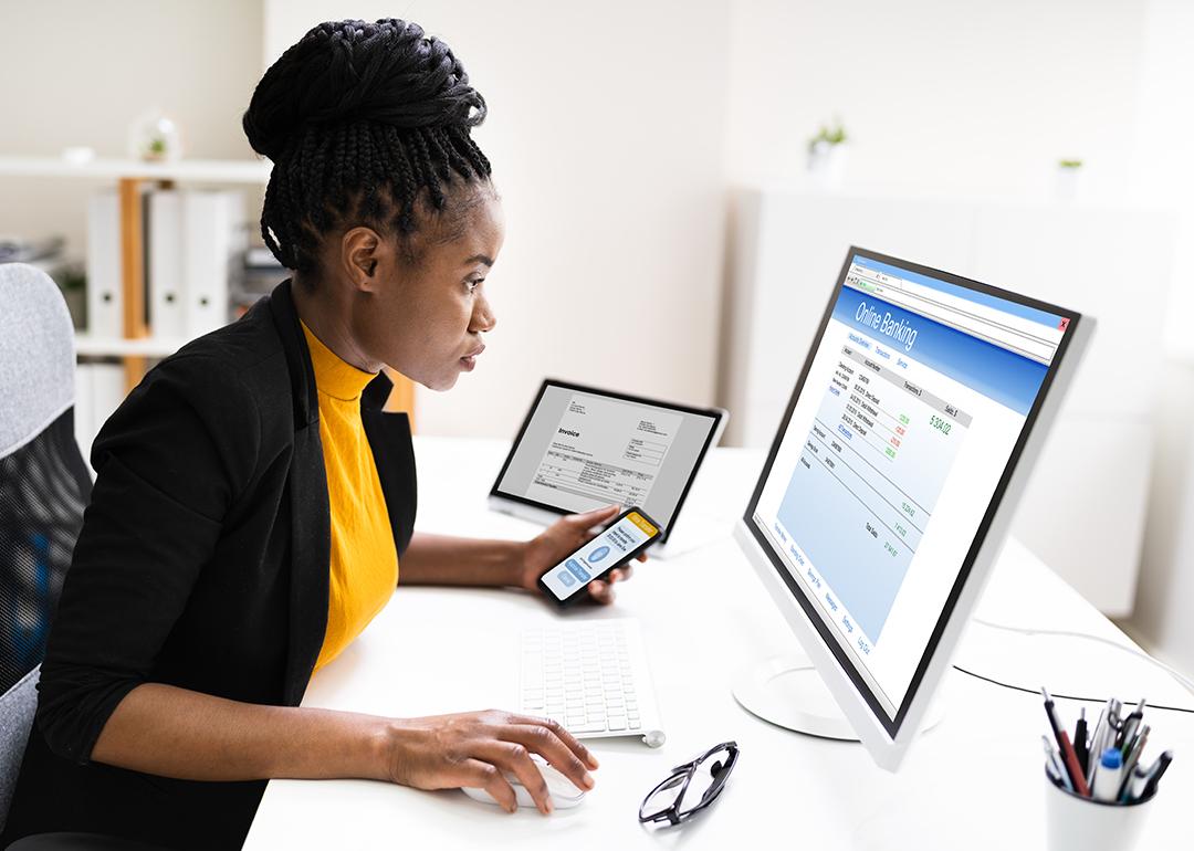 Woman using a phone and computer to use online banking.