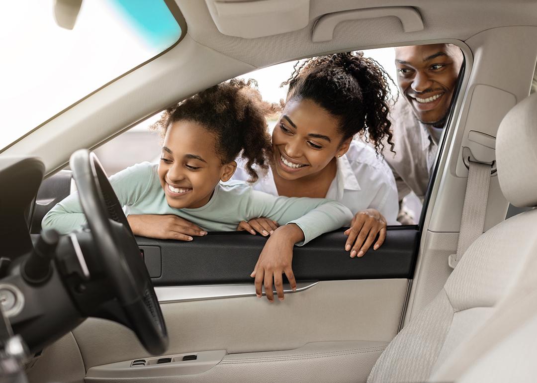 A family looking at the interior of a new car through its window.