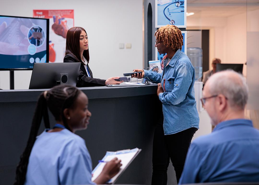 Patients and staff in a hospital reception desk area.