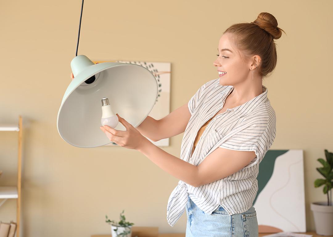 Young woman screwing light bulb into a ceiling lamp.