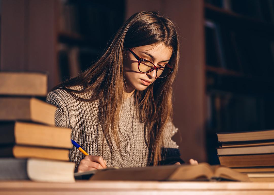 Young female student studying with a pile of books beside her.