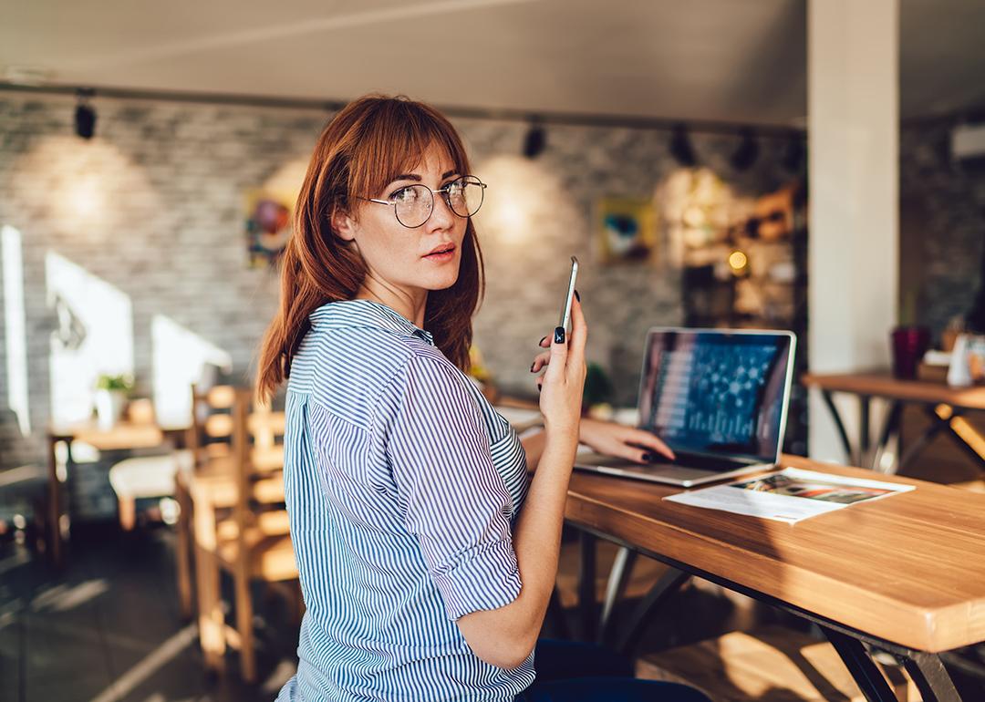 Woman looking at the camera while dialing a number on her mobile phone.