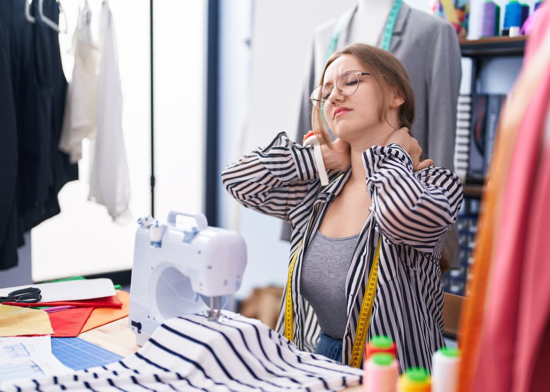 A tailoring shop owner holding the back of her neck from being tired and stressed.