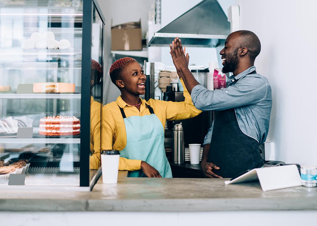 Cheerful black business owners giving high five to each other behind their store counter.