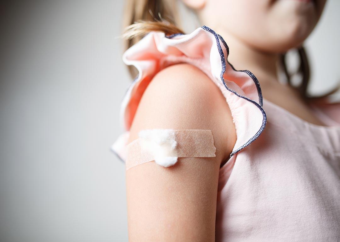Close up of child's upper arm with a cotton ball and tape covering vaccination site. 