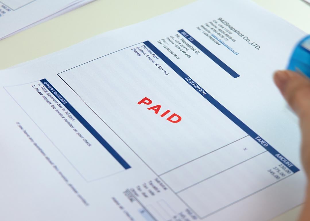 Worker sealing "paid" sign on an invoice document.