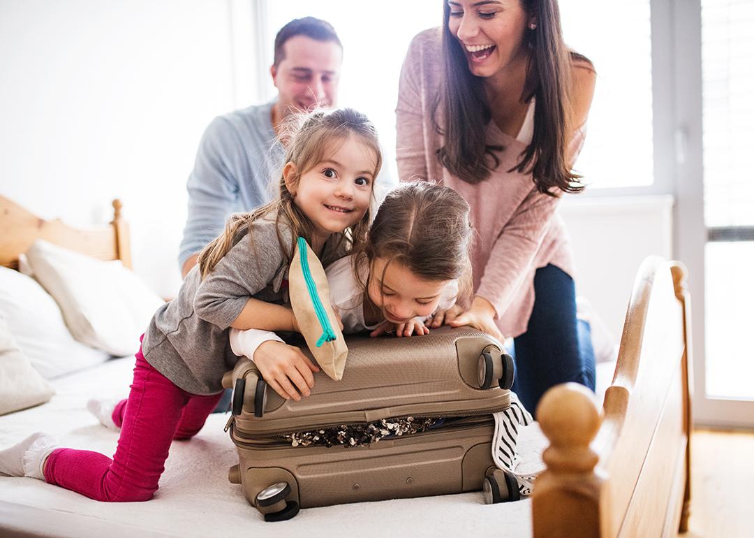 A happy family trying to close a packed suitcase.