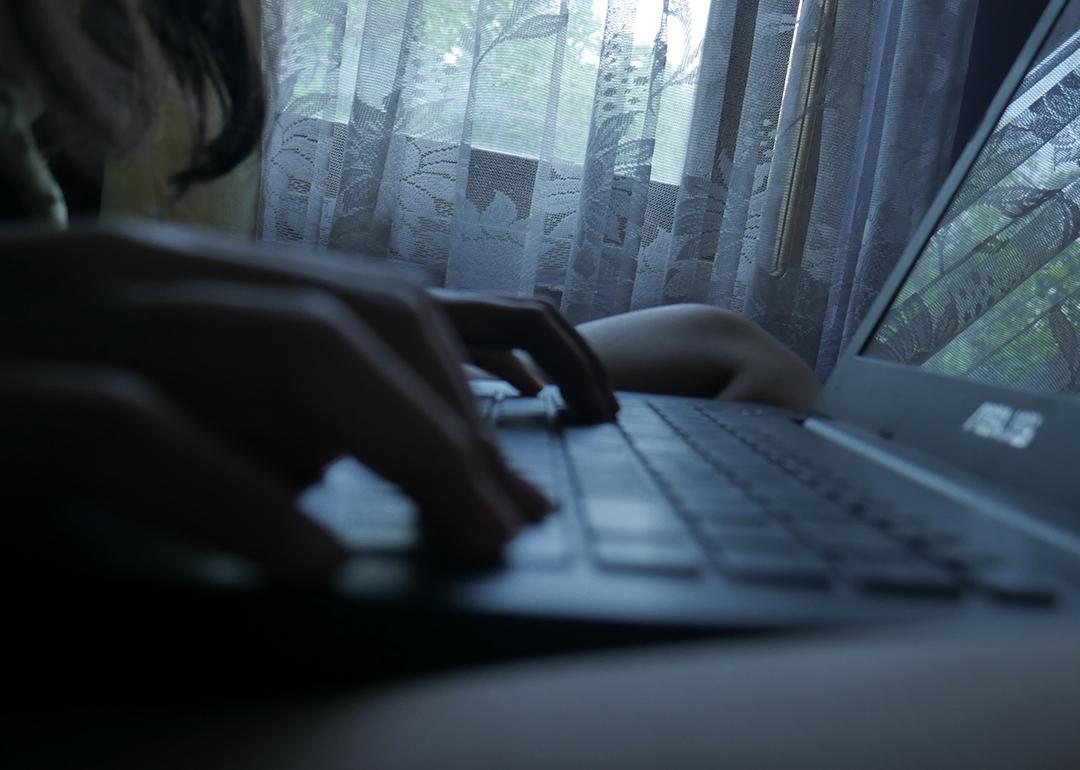 Silhouette of a person typing on a laptop at home.
