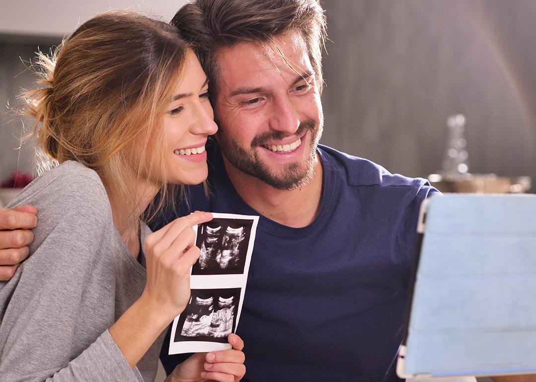 A young couple sharing ultrasound photographs while in a virtual call with loved ones.