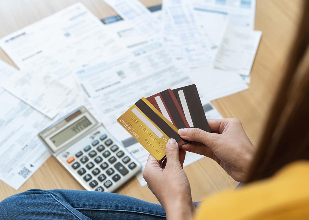 Young woman holding several credit cards and calculating a pile of bills.